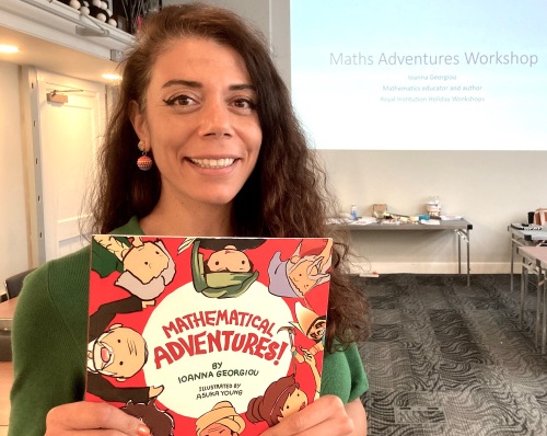 A young woman holds a book called Adventures in Mathematics